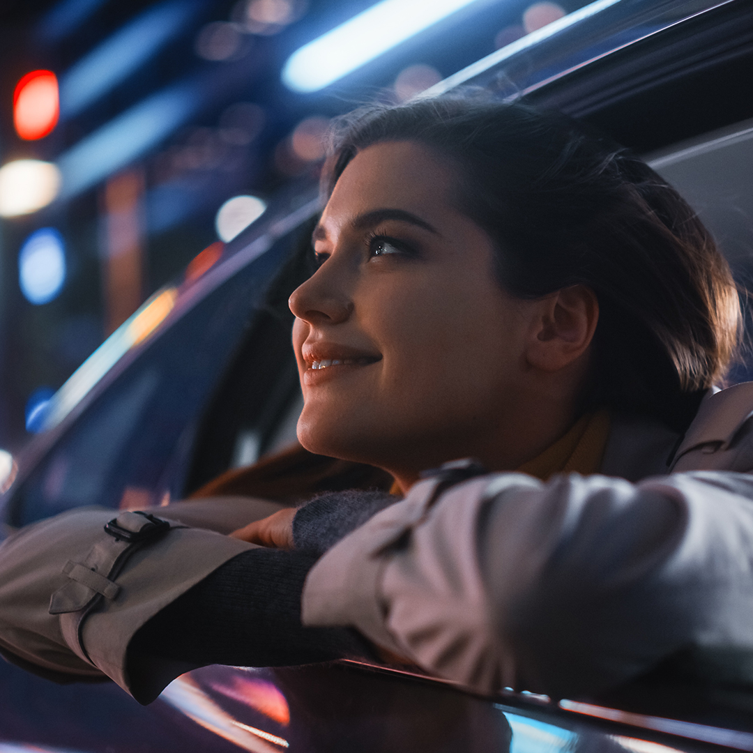 Smiling woman enjoying the vibrant nightlife of San Jose from a luxury limo window.